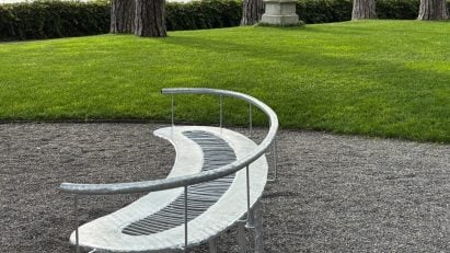 Steel bench on gravel in front of lawn with lake in background