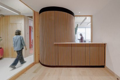 Reception desk attached to a large cylindrical column wrapped in vertical wood slats