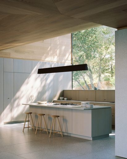 A kitchen bathed in light from a huge picture window made possible by a curved roofline