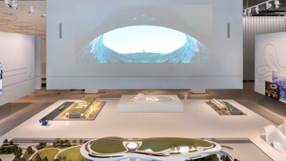 Wide view of the exhibition setup with large-scale models and projection screen
