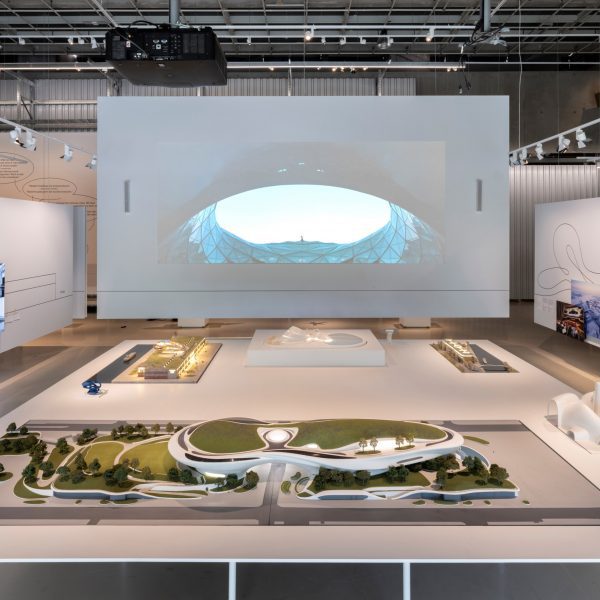 Wide view of the exhibition setup with large-scale models and projection screen