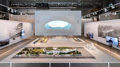 Wide view of the exhibition setup with large-scale models and projection screen