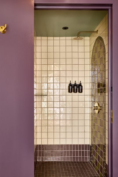 Shower with square beige tiles behind a purple door frame
