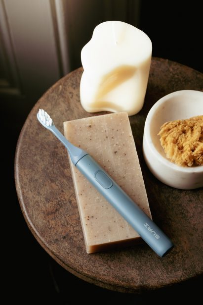 Photo of a navy blue Suri toothbrush sat on a side table on top of a clean rectangular bar of soap and other textured ornaments