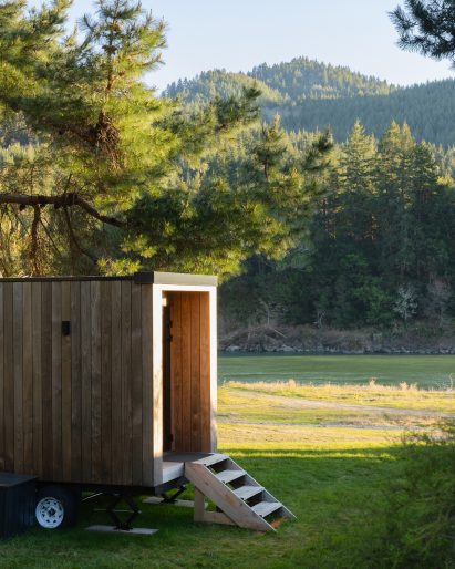 A small wooden sauna with forested mountains in the background