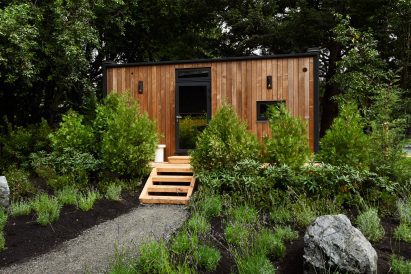 Back side of a mirrored cabin with a wooden facade and steps up to the door