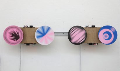 Spinning pink, blue, white and brown discs mounted onto a wall