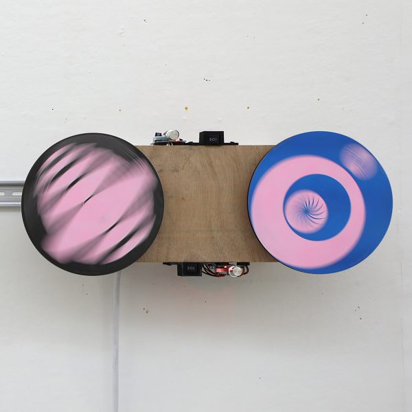 Spinning pink, blue, white and brown discs mounted onto a wall