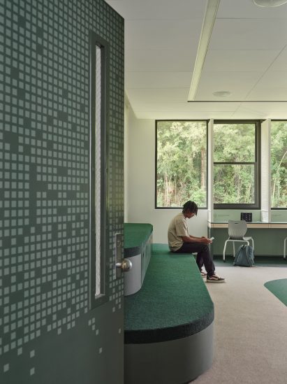 View through an open door into a classroom, where a boy is sat on a green bleacher seat