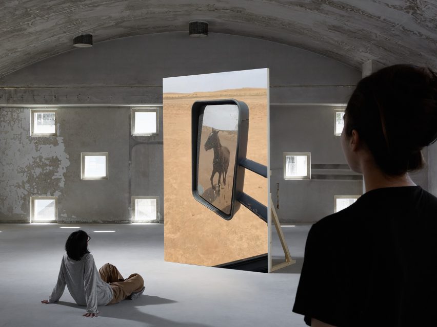 Photo of the Who Stole the Sky video installation by Ze Qiu showing a portrait-orientated large screen with an image on it of a horse traversing a desert landscape as seen through a car's side mirror. People are watching the work