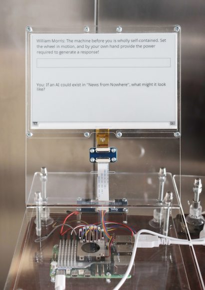 Close-up photo of an e-paper screen with writing on it above a steampunk-like hardware set-up for the Prompting Nowhere project