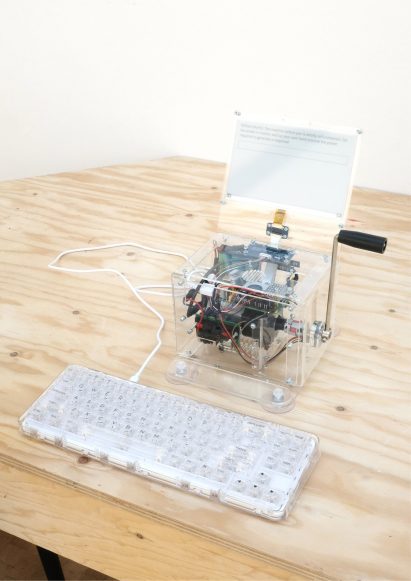 Photo of a small computer within a perspex box attached to a hand crank and an external keyboard