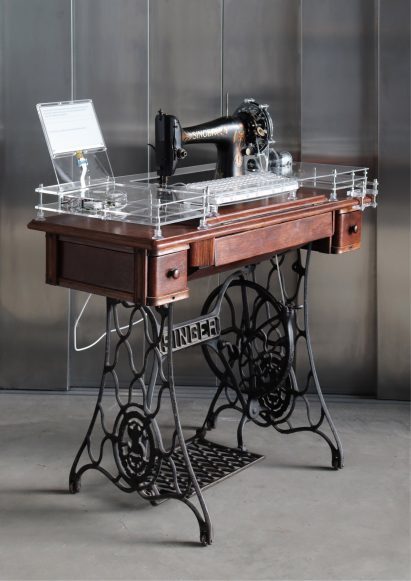 Photo of an old Singer treadle sewing machine modified to have a perspex top with computer components inside running a local AI