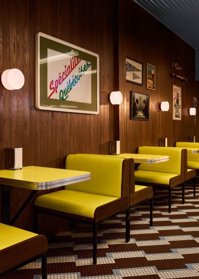 Row of bright yellow booth seating and matching tabletops against a dark wood wall