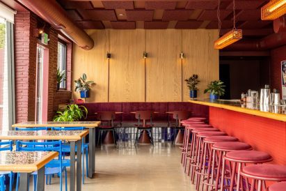 Bar interior with blue chairs against dining tables and red stool along the bar