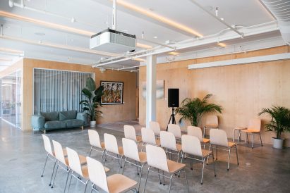 Event space set up for a presentation, featuring plywood walls and concrete flooring