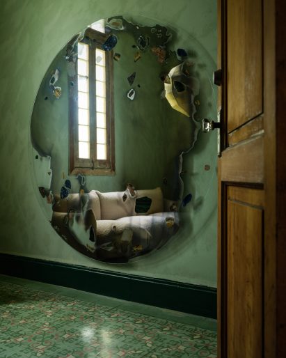 A large mirror by Chen Chen and Kai Williams reflects a boucle sofa by Mario Marenco in a green room