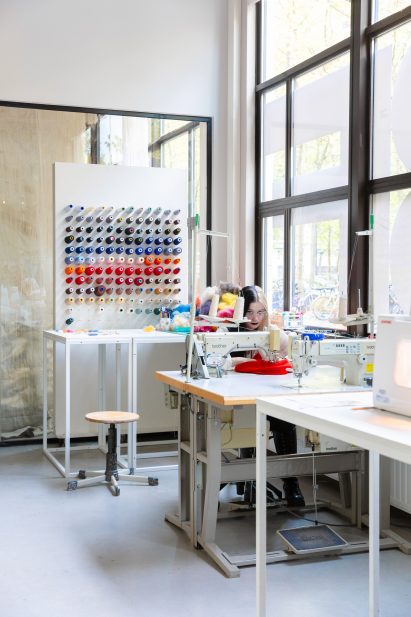 Photo of a person at work in a sewing station within an exhibition space at the New Order of Fashion LAB