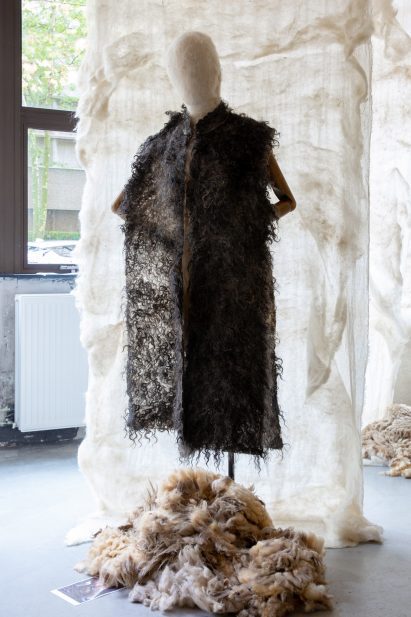 Photo of a long jacket made from dark curly wool by Shushanik Droshakriyan displayed in an exhibition