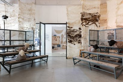 Photo of a room set up for talks within an exhibition featuring tiered bench seating with abstract stuffed sheep scattered on the seats