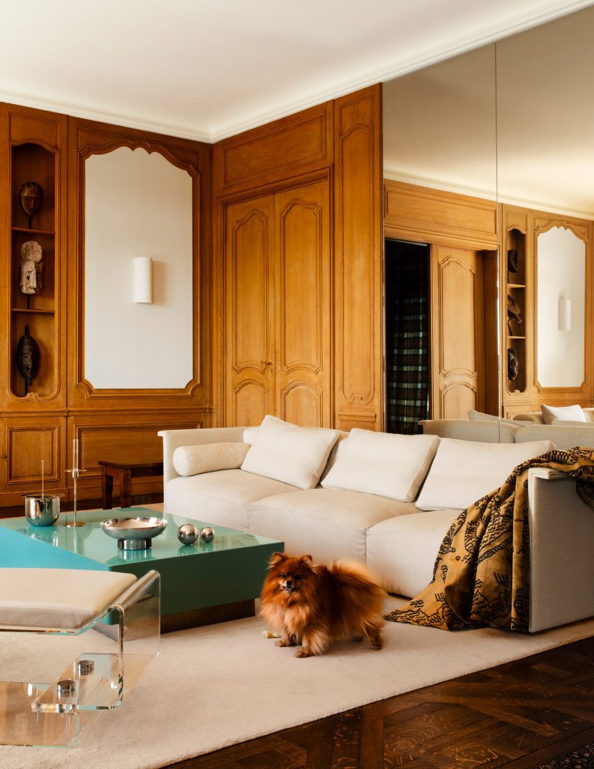 Photograph of the living space, showing a modular white sofa. There is a small dog in the photo.