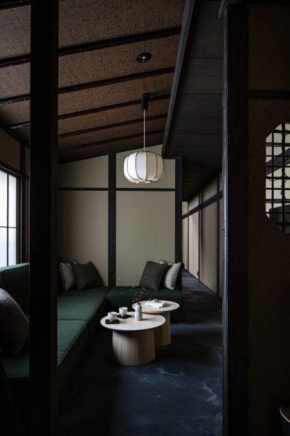 Photograph showing an L-shaped seating area, complete with cushions and two circular coffee tables. A pendant light with a paper-lampshade hangs from the ceiling above the tables.