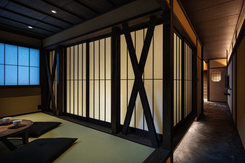 An image displaying large, washi-paper doors with dark wooden borders. There is a corridor going down the right side of the image and a small table with two futon-pillows on the floor for sitting.