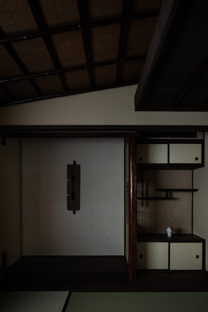 A photo containing a display shelf with in-built storage cabinets on the right side, and a beige wall on the left with a central light-fixture. There is a slanted ceiling with dark wooden beams at the top of the photo.
