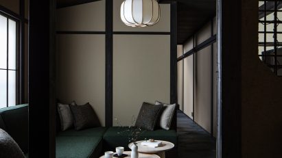 Photograph showing an L-shaped seating area, complete with cushions and two circular coffee tables. A pendant light with a paper-lampshade hangs from the ceiling above the tables.
