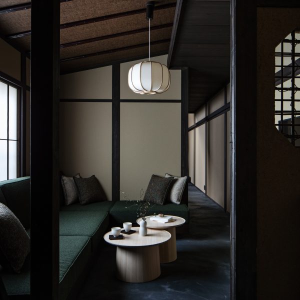 Photograph showing an L-shaped seating area, complete with cushions and two circular coffee tables. A pendant light with a paper-lampshade hangs from the ceiling above the tables.