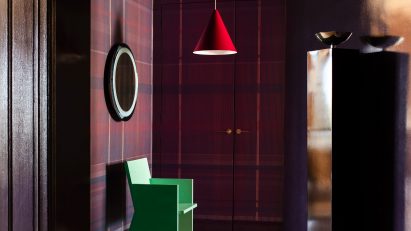 Photograph of the dramatic entrance hall, which has tartan wallcoverings in a deep purple. There is a patterned marble floor, and a green sculptural chair, spotlighted by a red-hanging pendant light.