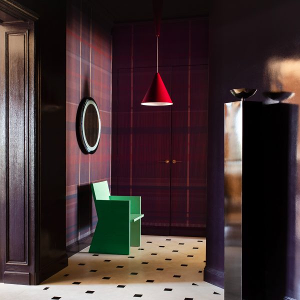 Photograph of the dramatic entrance hall, which has tartan wallcoverings in a deep purple. There is a patterned marble floor, and a green sculptural chair, spotlighted by a red-hanging pendant light.