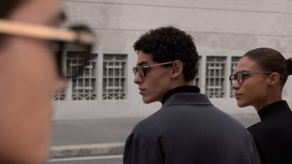 Photo of a man and a woman on the street wearing versions of the Even Realities Even G2 glasses, while another wearer is blurred in the foreground