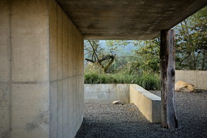 Concrete passageway with a wooden support post, opening onto gravel and greenery outside the structure