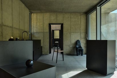 Minimalist interior with exposed concrete walls, black modern furniture and large windows overlooking an outdoor gravel area