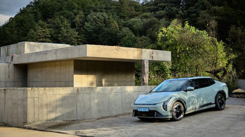 Kia EV4 parked beside a minimalist concrete bathhouse building, surrounded by trees and greenery