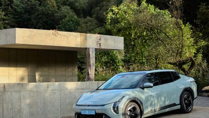 Kia EV4 parked beside a minimalist concrete bathhouse building, surrounded by trees and greenery