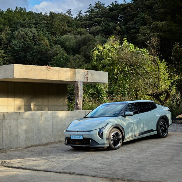 Kia EV4 parked beside a minimalist concrete bathhouse building, surrounded by trees and greenery
