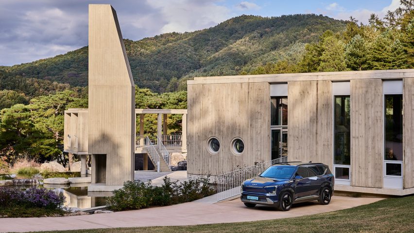 Kia EV5 parked in front of a minimalist concrete building set within a forested mountain landscape