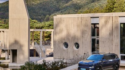 Kia EV5 parked in front of a minimalist concrete building set within a forested mountain landscape