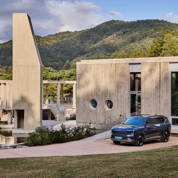 Kia EV5 parked in front of a minimalist concrete building set within a forested mountain landscape