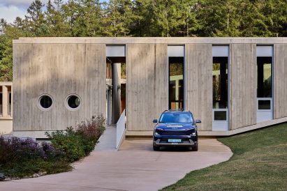 Kia EV5 positioned in front of a tall, narrow concrete facade with circular and vertical windows