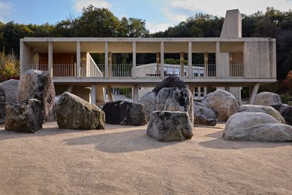 Large natural boulders arranged beneath an elevated concrete walkway supported by cylindrical pillars