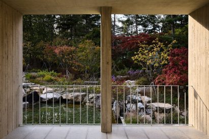 View through a concrete-framed opening looking out onto a landscaped garden with rocks and colourful autumn foliage