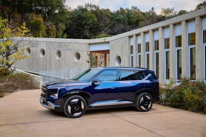 Kia EV5 parked beside a long concrete structure with circular windows, surrounded by autumn trees