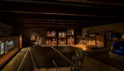 A dark room with a doll collection and a desk with paints on display