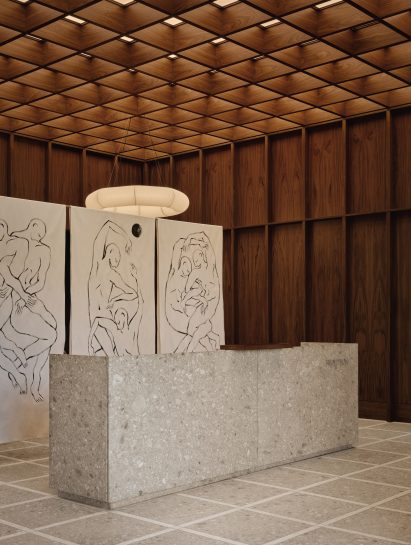 A terrazzo reception desk in front of a trio of panels adorned with figurative drawings