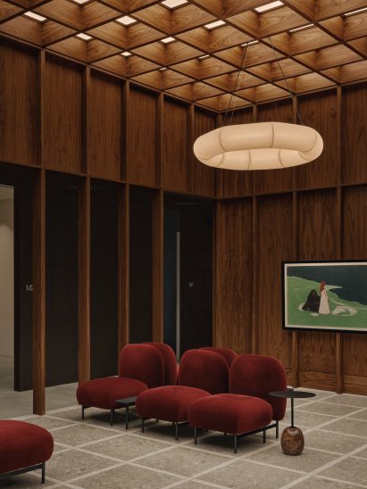 A skylight brings diffused light into a double-height waiting area, furnished with red velvet club chairs