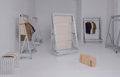 Minimalist industrial furniture installation featuring steel and wood modular frames on caster wheels in a white gallery space.
