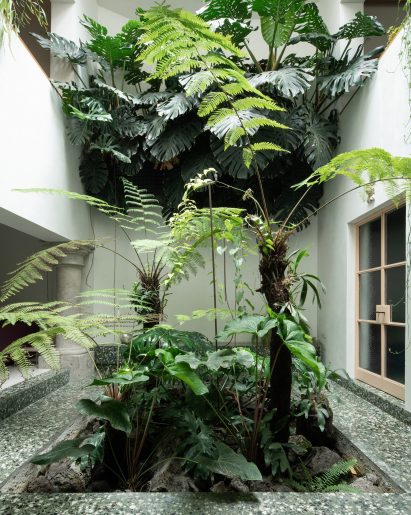 An atrium filled with tropical plants, with green terrazzo around the base